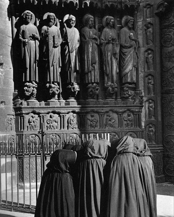 Four women in headscarves bowing in front of detailed medieval stone statues, a weird history pic showing past religious practices.