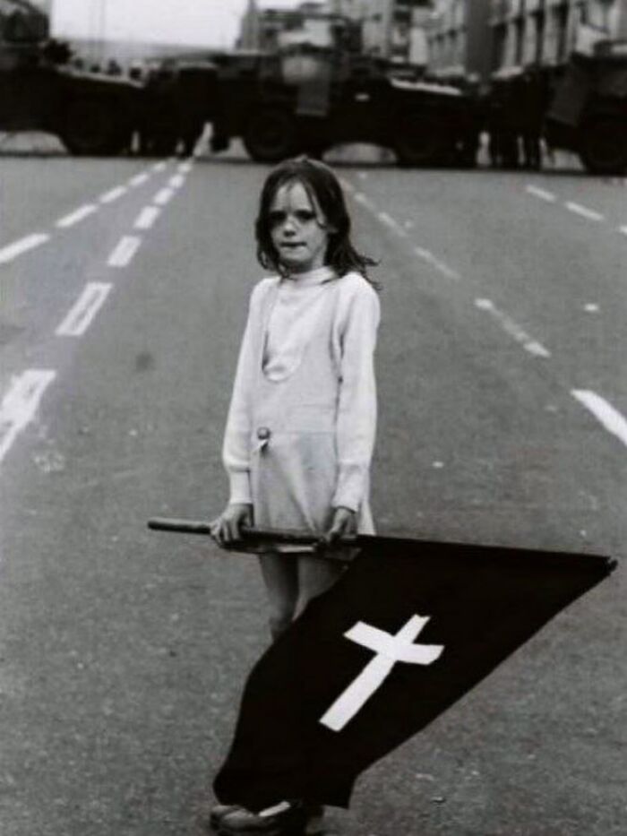 Young girl holding a flag with a cross standing on an empty street in a powerful weird history photo.