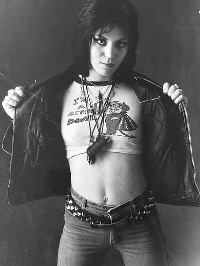 Young woman in leather jacket revealing a cropped cartoon devil shirt, showcasing weird history fashion in black and white.