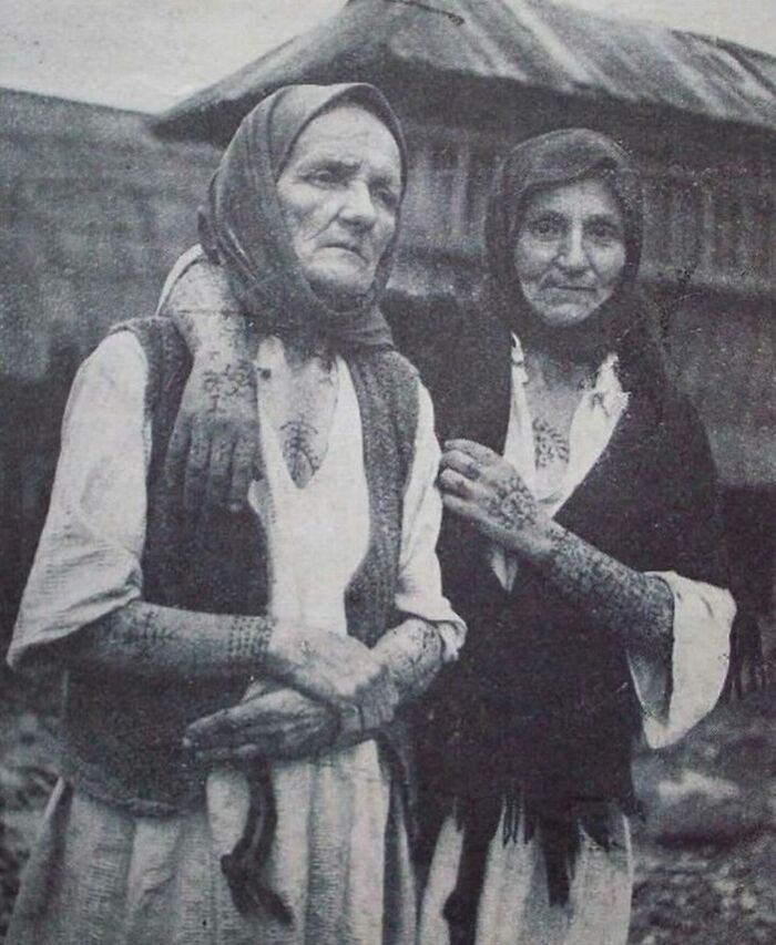 Two elderly women with traditional tattoos on arms and hands, wearing headscarves in a weird history photo from the past.