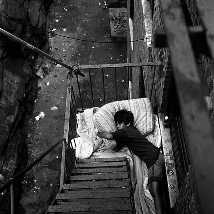 Boy sleeping on a makeshift bed on a fire escape, showcasing weird history moments that change how we see the past.