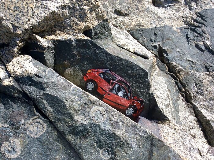 Street art photo of a red car painted on rocky surface blending with natural stone formations.