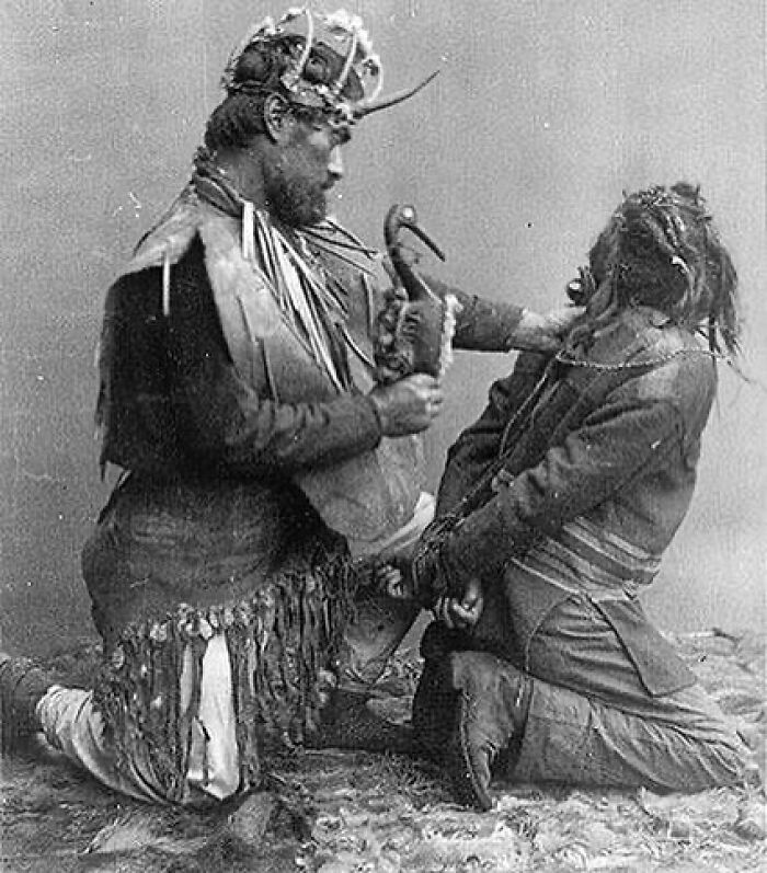 Black and white weird history pic showing two men in traditional attire interacting in a dramatic pose from the past.