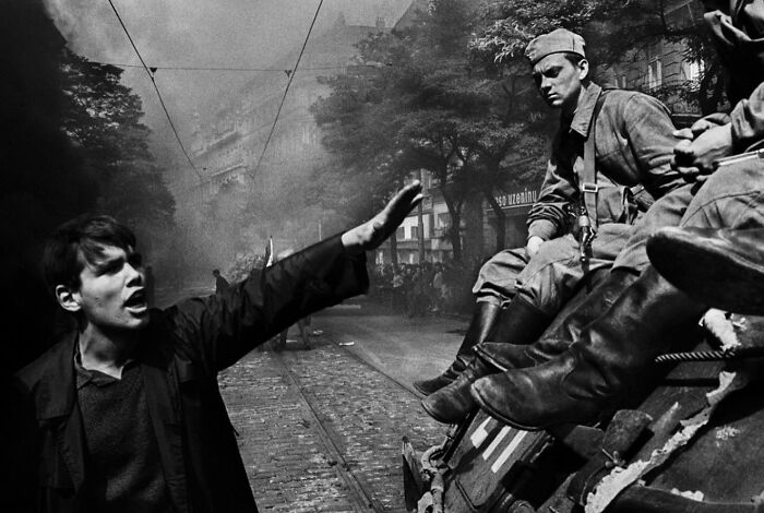 Black and white weird history photo showing a young man confronting soldiers on a street during a past conflict.