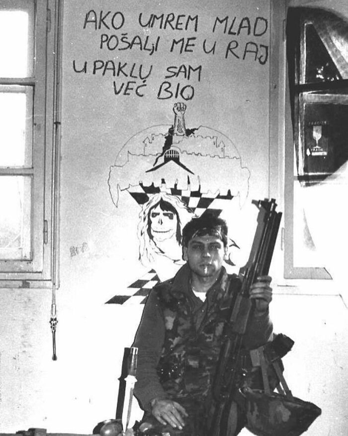 Black and white photo of a soldier holding a rifle, sitting in front of a wall with distinctive graffiti in weird history pics.