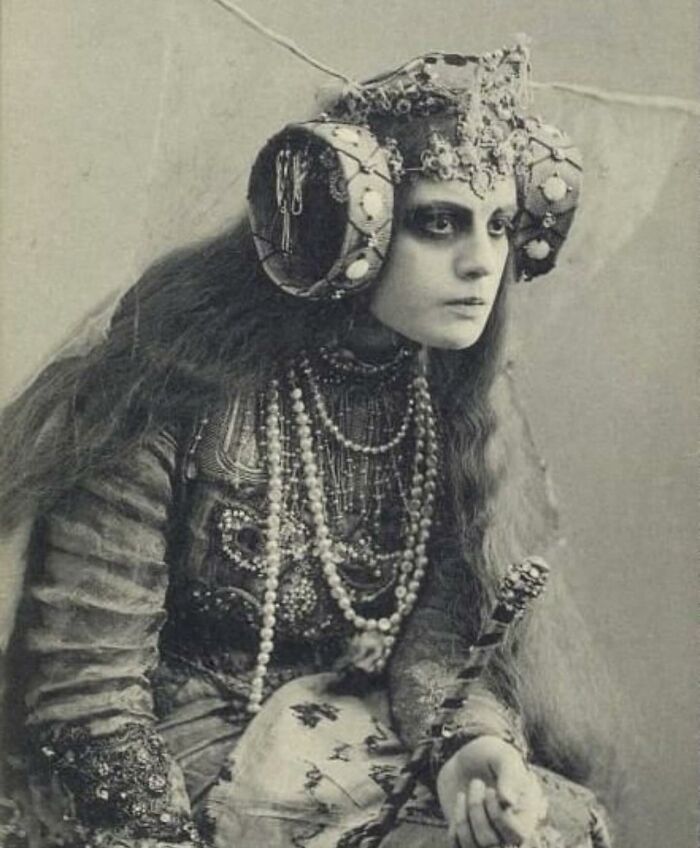 Black and white photo of a woman in an elaborate historical costume with pearls and an unusual headdress from weird history pics.