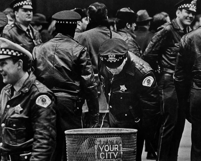 Black and white photo of Chicago police officers in leather jackets surrounding a trash can, a weird history pic from the past.