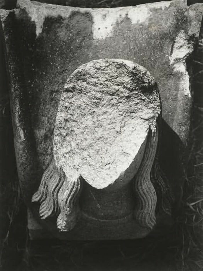 Eroded stone statue head with carved hair, showcasing a weird history artifact from the past in black and white.