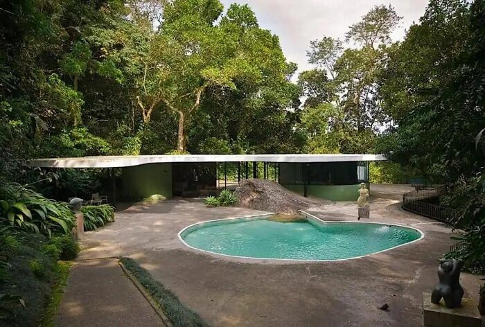 Modern iconic architectural homes featuring a minimalist design surrounded by lush greenery and a curved swimming pool.