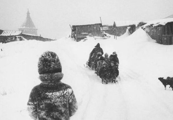 Children sledding down a snowy hill in a historic village, showcasing a weird history moment from the past.