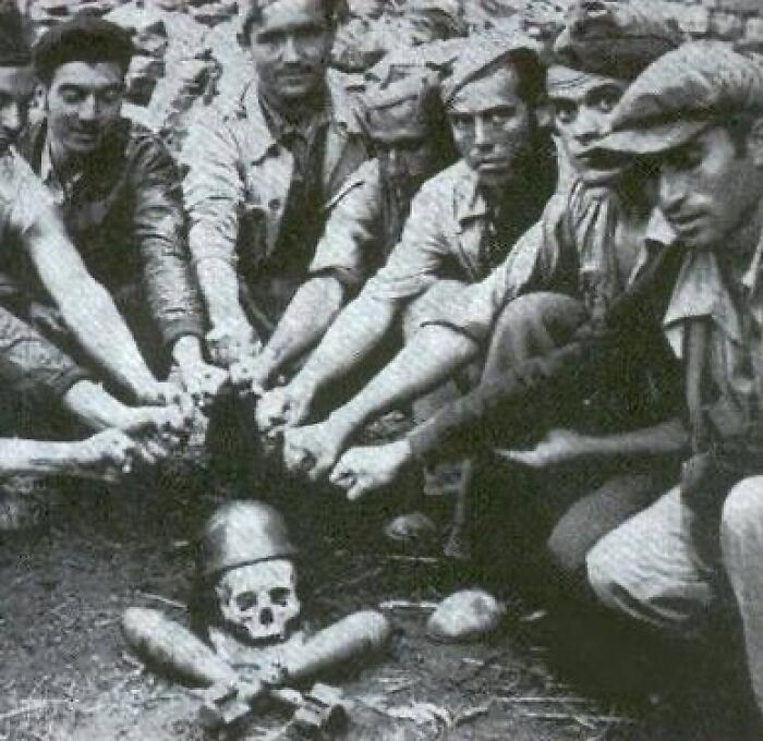 Group of men in early 20th century attire gathered around and pointing at an unusual human skull, weird history photo.