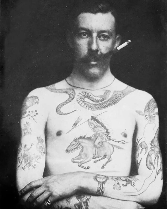 Black and white image of a tattooed man smoking with weird history pics showing detailed body art from the past.