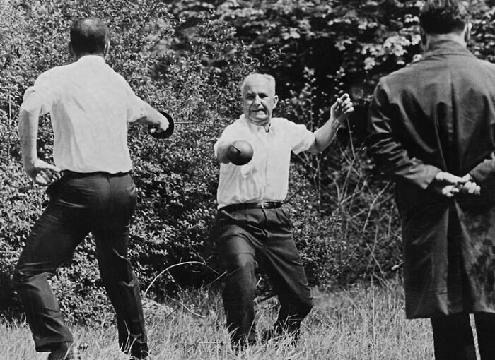 Black and white weird history photo showing men in vintage clothing playing a game with balls in an outdoor grassy area.