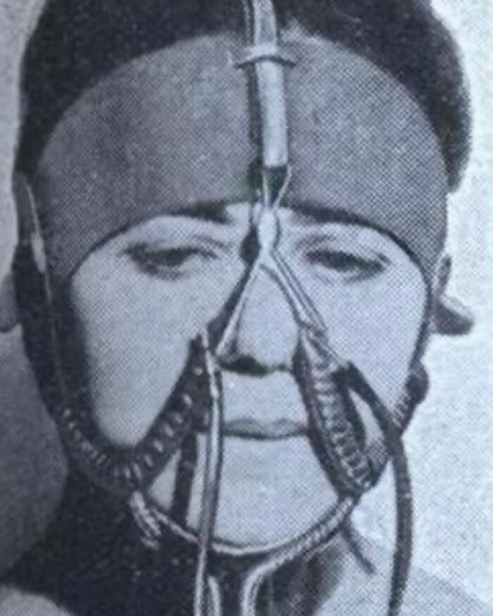 Black and white vintage photo of a man wearing an unusual headgear device in a weird history pic.