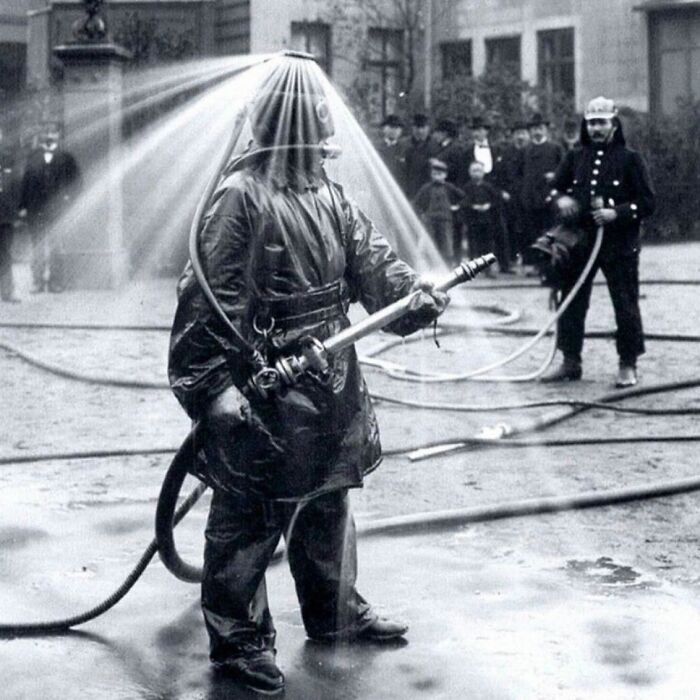 Firefighter in early protective gear with water spraying over helmet, showcasing weird history pics of firefighting equipment.