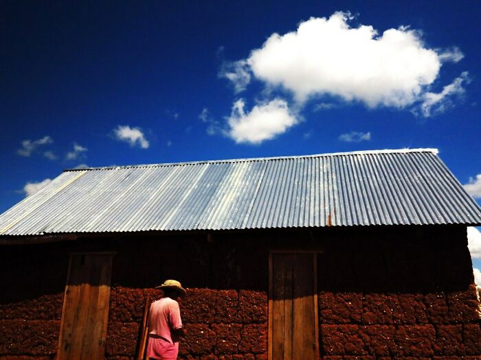 Person wearing a hat standing near a rustic building under a bright blue sky in street photos capturing everyday life.