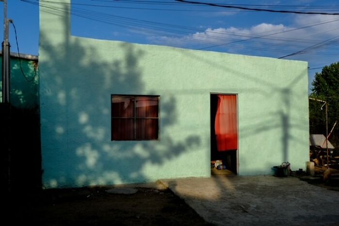 Simple turquoise house with red curtain in doorway, showcasing everyday life in a street photo by Stéphane Kyndt.