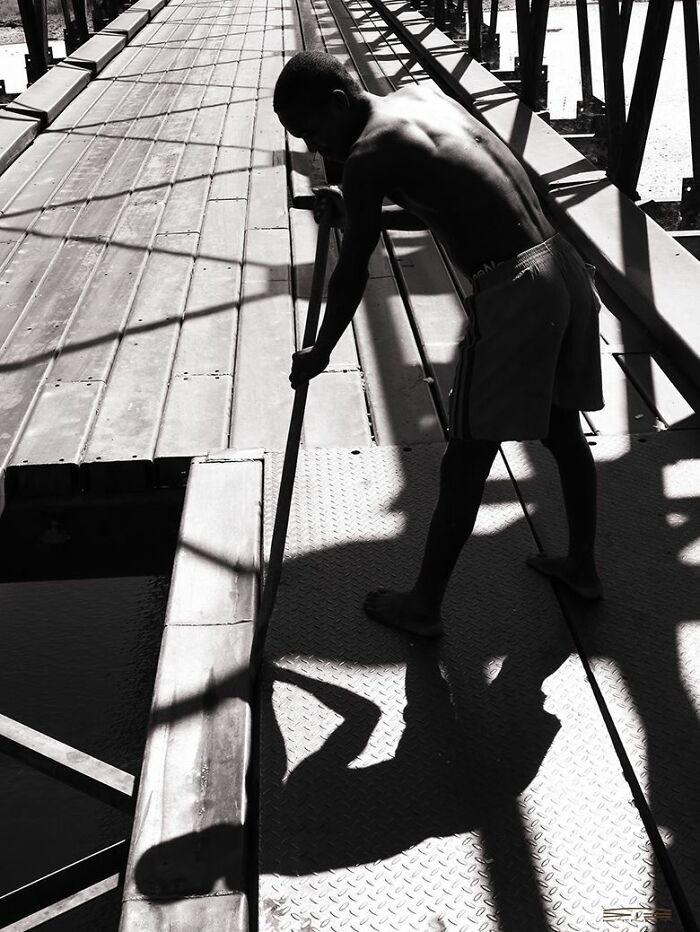 Black and white street photo showing a boy cleaning a metal walkway, capturing everyday life moments in urban settings.