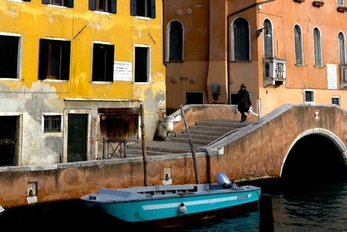 Colorful street scene featuring a pedestrian on a bridge and a boat in the canal captured in street photography.