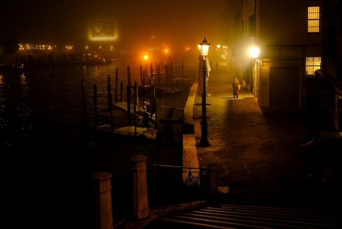 Night street scene with glowing lamps and a person walking near boats in street photos showing everyday life.