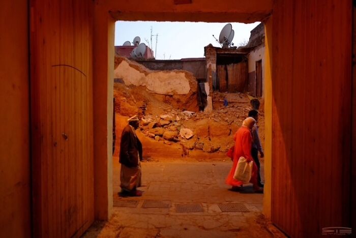 Street photo capturing everyday life with people walking through an old alley under warm orange lighting at dusk.