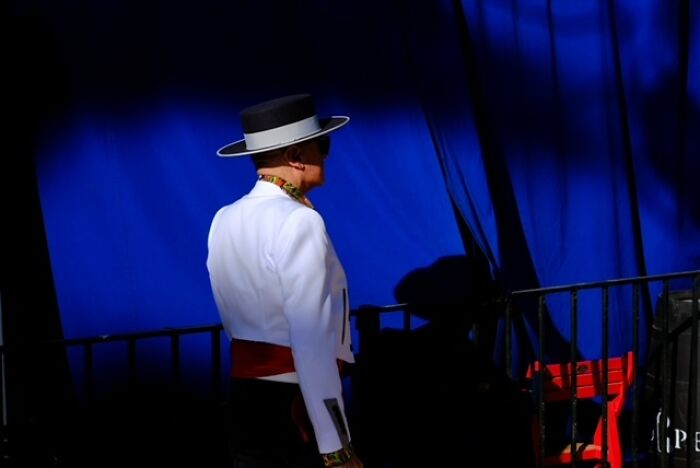 Man in traditional attire with a wide-brim hat standing against a deep blue background street moments captured