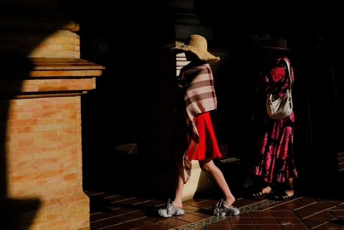 Two women in contrasting light, one wearing a straw hat and red skirt, captured in street photos showing everyday life.