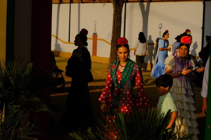 Street photo capturing everyday life with people dressed in traditional attire during a sunny outdoor event.