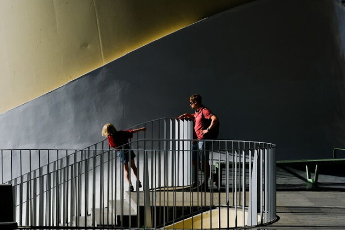 Two people captured on the streets, standing on a curved metal railing, with strong light and shadow contrast.