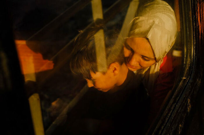 Woman wearing a headscarf embracing a child inside a dimly lit vehicle, street photo capturing everyday life moments.