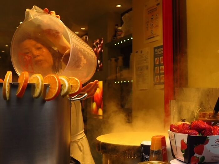 Woman pouring liquid into a pot decorated with orange slices, capturing everyday life in a street photo by Stéphane Kyndt.