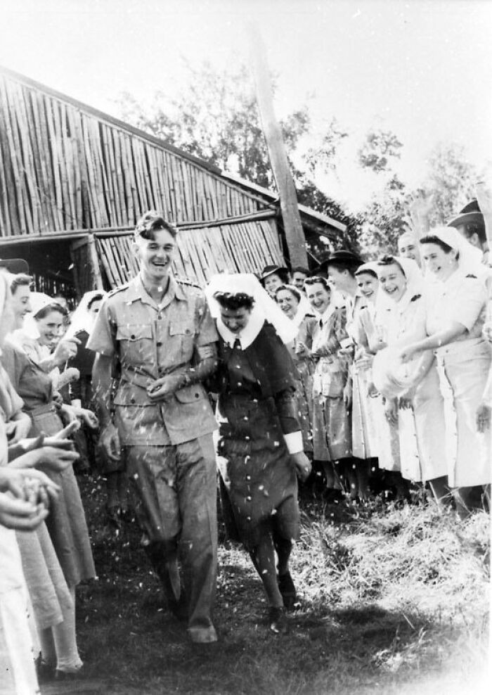 Smiling couple in 1940s wedding attire walking through cheering crowd in a moving wedding photo from the war era.