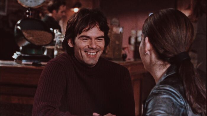 Actor smiling and talking to a woman in a cozy setting, capturing the charm of iconic heartthrobs from their time.