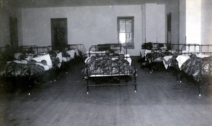 Dormitory room with multiple metal beds and sleeping children in Native American boarding schools from the 1910s.