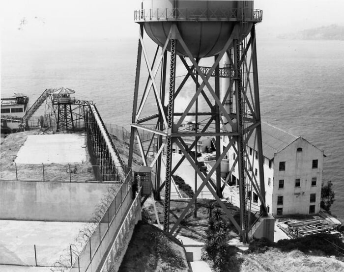 Black and white photo of a guarded fence and water tower illustrating the harsh reality of life on Alcatraz prison island.