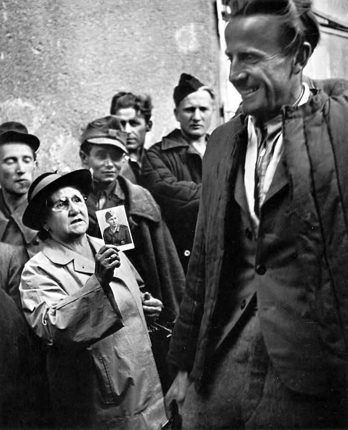 Black and white photo showing a woman holding a soldier's portrait among a group, capturing iconic moments in history.