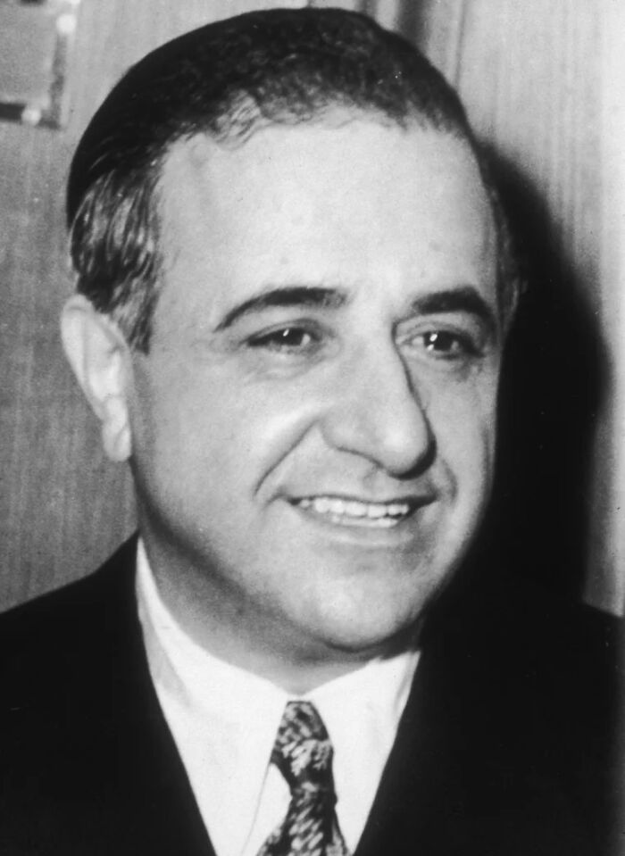 Black and white portrait of a smiling mob boss in suit and tie, representing notorious mob bosses known worldwide.