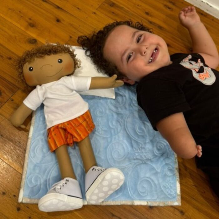Child lying next to a doll designed to fit rare health conditions, representing unique needs with care and detail.