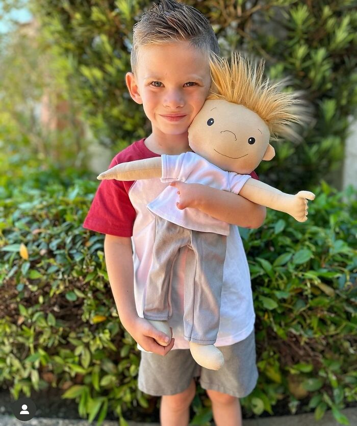 Young boy holding a custom doll designed to represent a child's rare health condition and specific needs outdoors.