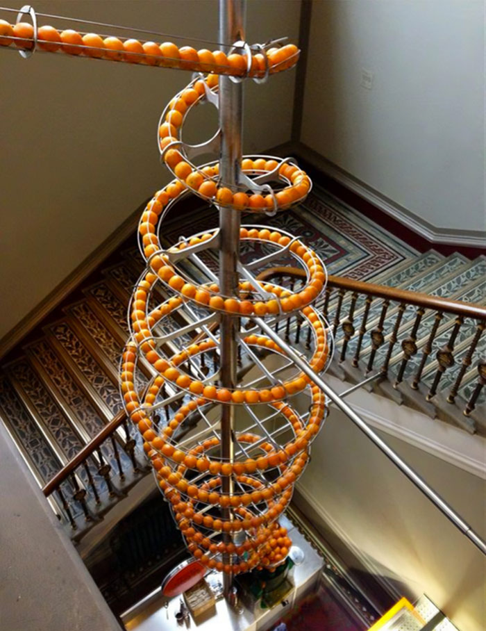 Spiral installation with orange balls in a creatively designed bar or restaurant space with decorative stairs.