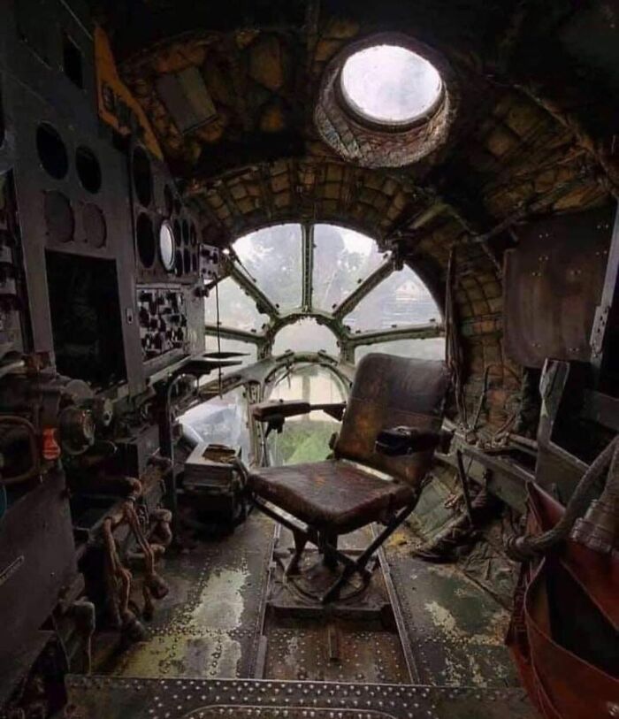 Interior of an old airplane cockpit with worn controls and a single chair, revealing unfamiliar parts of history.