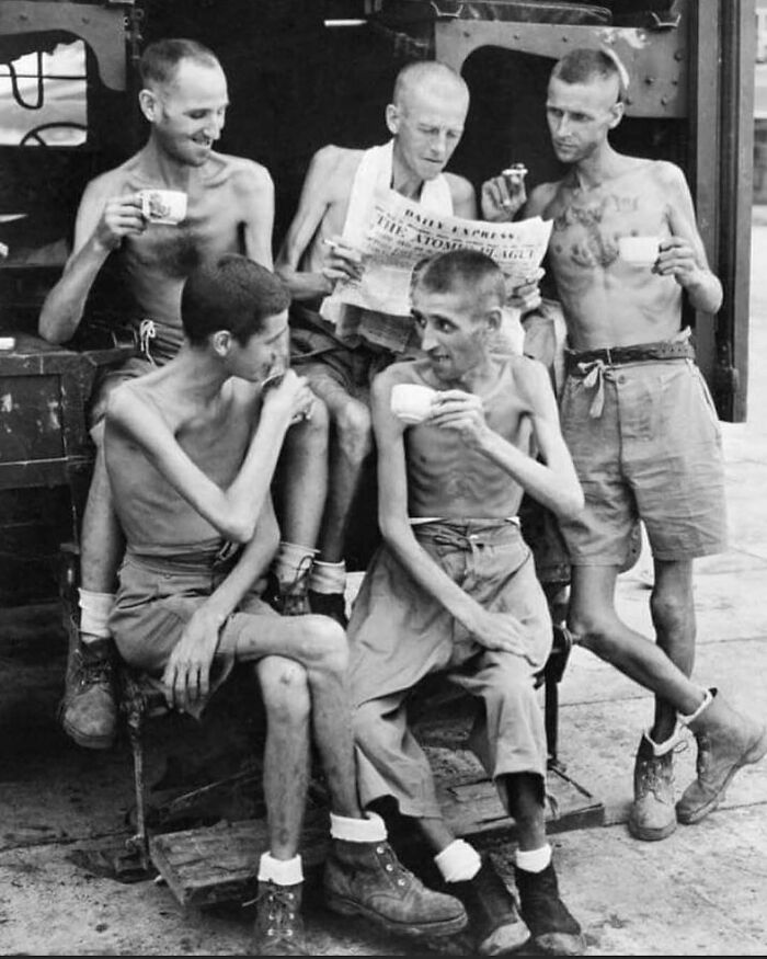 Group of malnourished men drinking tea and reading a newspaper, highlighting unfamiliar parts of history in a black and white photo.