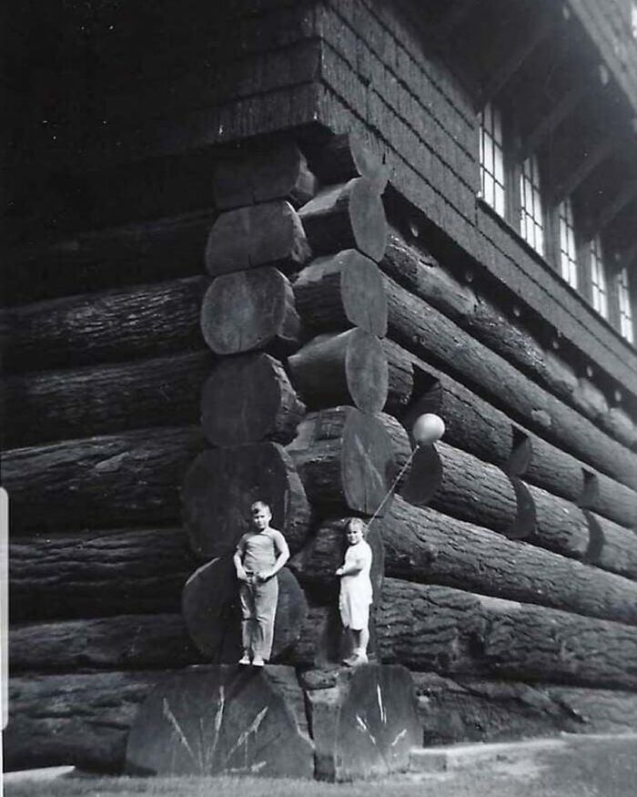Two children standing by massive log cabin illustrating unfamiliar parts of history and old construction techniques.