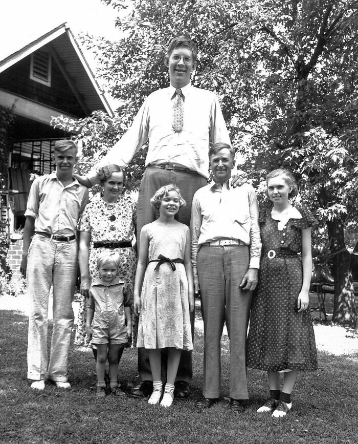 Tall man standing with family members outside a house, illustrating unfamiliar parts of history through a vintage black and white photo.