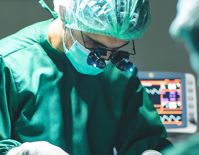 Surgeon wearing magnifying glasses and surgical gear during an operation, illustrating new facts in medical practice.