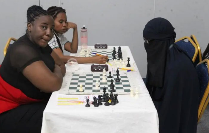 Three women playing chess in a tournament setting, focused on the game and sharing new facts about strategies.