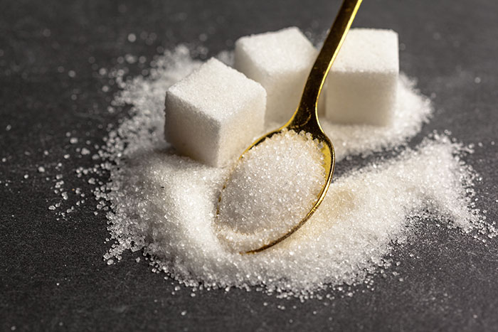 Close-up of white sugar cubes and granulated sugar on a gold spoon, illustrating new facts about sugar use.