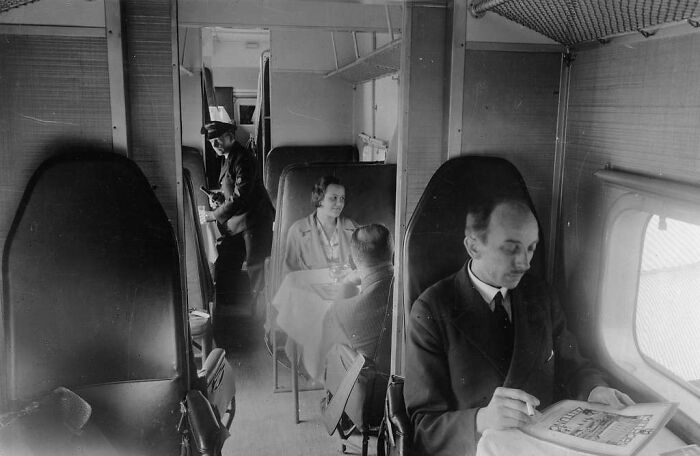 Vintage black and white photo showing glamour of flying with passengers dining and relaxing in an elegant airplane cabin.