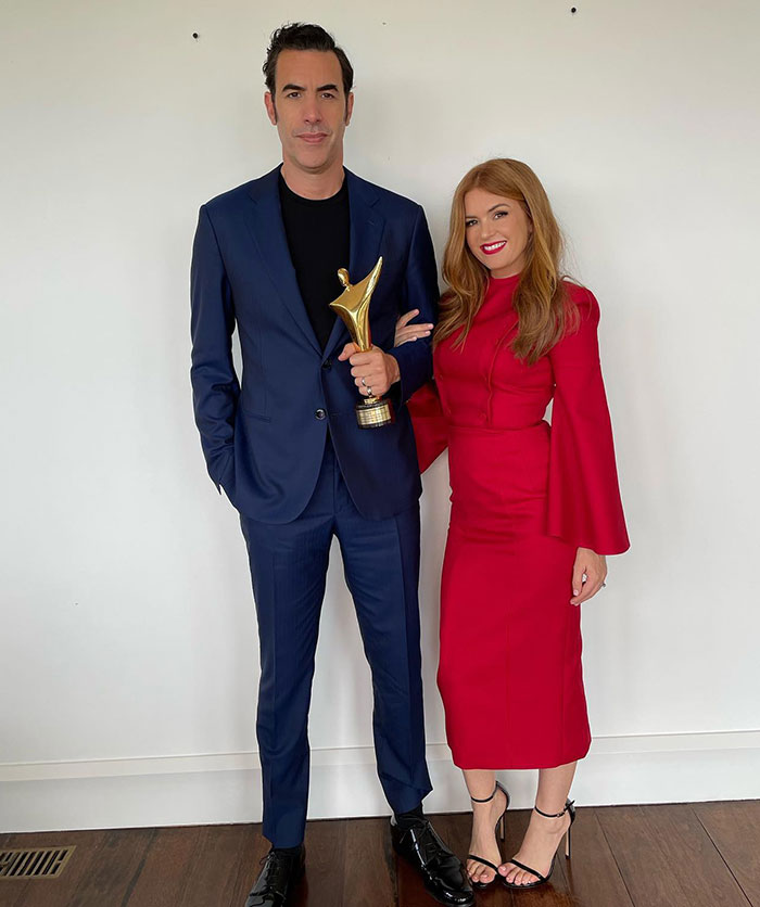 Isla Fisher and Sasha Baron Cohen posing indoors, with Isla in a red dress, amid news of tough couple of years. - 16