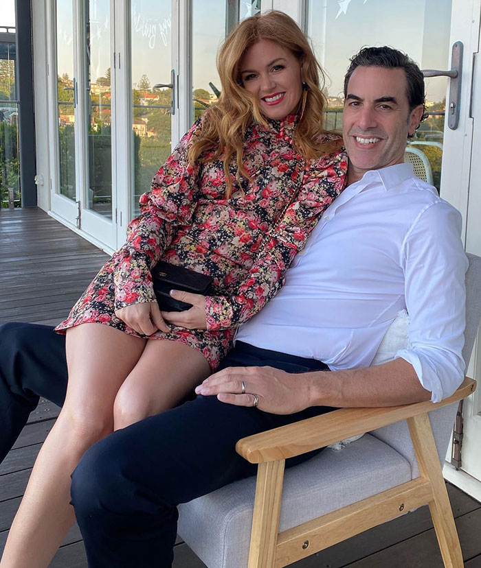 Isla Fisher smiling in floral dress sitting with Sasha Baron Cohen on a chair during a casual outdoor moment. - 13